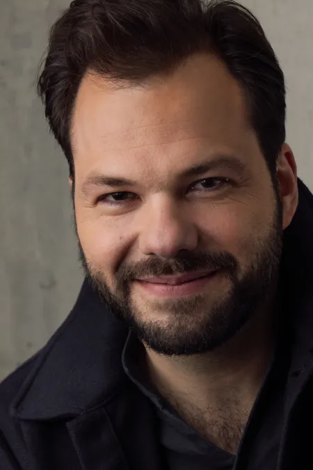 © Susanne Hassler Smith Porträt von Dirigent Petr Popelka mit kurzem dunklem Haar und Bart, lächelnd, vor hellem Hintergrund