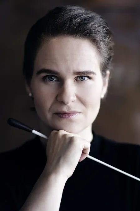 © Nikolaj Lund Person mit zurückgebundenem Haar hält einen Dirigentenstab vor dem Kinn, trägt schwarzen Pullover